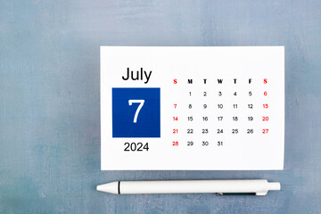 July Calendar 2024 page with pen on wooden background.