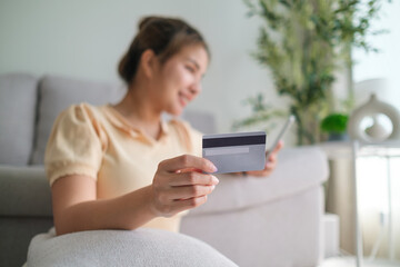 Happy young woman holding credit card  and mobile phone while paying bill or shopping online at...