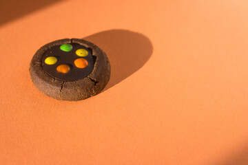 Brown cookie with colourful drops on peach fuzz baclground. Chocolate biscuit in sunlight on orange...
