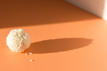 Creamy candy on peach fuzz background. Coconut raffaello on peach color banner. Raffaello ball in sunlight. Simplicity concept. Sweet dessert isolated. Praline candy in sunshine with shadow.