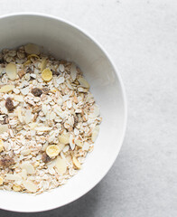 Top view of oat muesli in a white ceramic bowl, overhead view of muesli with oats almonds raisins and cornflakes in a white breakfast bowl
