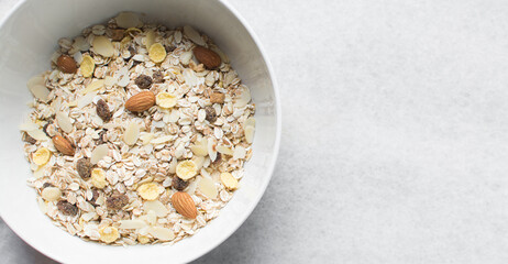 Top view of oat muesli in a white ceramic bowl, overhead view of muesli with oats almonds raisins and cornflakes in a white breakfast bowl, prepping healthy granola breakfast bowl