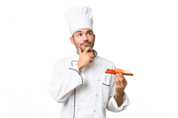 Young caucasian chef holding a sushi over isolated background having doubts