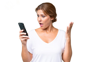 Fototapeta premium Middle-aged caucasian woman over isolated background looking at the camera while using the mobile with surprised expression