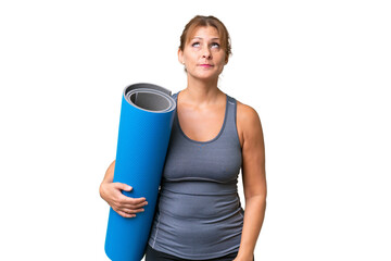 Middle-aged sport woman going to yoga classes while holding a mat over isolated background and...