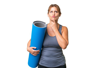 Middle-aged sport woman going to yoga classes while holding a mat over isolated background having...