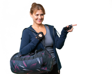 Middle-aged sport woman with sport bag over isolated background pointing finger to the side and presenting a product