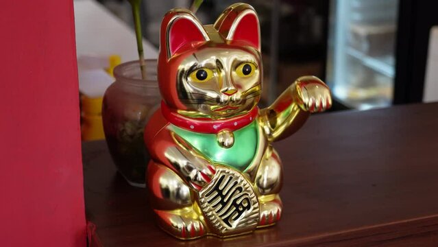 4k video footage of Chinese Golden cat figurine with one paw raised in a beckoning gesture on working table or shop cashier desk. Japanese Maneki-neko or Lucky Cat Statue.