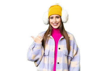Young woman wearing winter muffs over isolated chroma key background pointing to the side to present a product