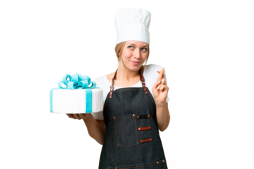 Young pastry blonde woman with a big cake over isolated chroma key background with fingers crossing and wishing the best