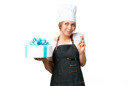 Young pastry blonde woman with a big cake over isolated chroma key background with fingers crossing and wishing the best