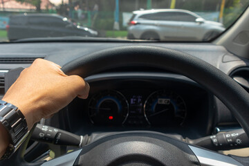 Hand of man holding steering wheel of car with one hand