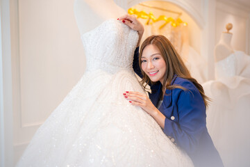 Attractive young bride is smiling while choosing wedding dress in modern wedding salon.
