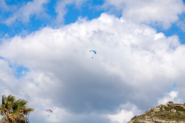 Two paragliders flying in the sky above mountain and palm tree