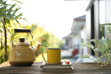 Yellow cup and tea pot and on wooden tray and plant pot on wooden table