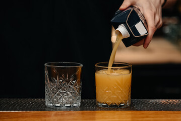 bartender pours orange juice into one of two glasses on bar stand, background, nightlive concept