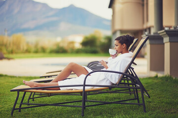 Woman, relax and tea in hotel outdoor in bathrobe for travel holiday at hospitality resort, morning...