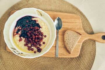 Top view of a plate of wheat porridge with red currants and blueberry jam. A plate of wheat porridge for a healthy gluten-free breakfast, next to a spoon and a piece of bread. High quality photo