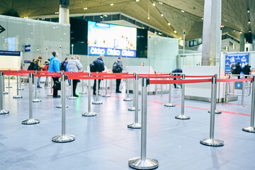 A red retractable barrier at the airport check-in desk. People are queuing up to register. High...
