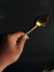 hand holding spoon gold color black background