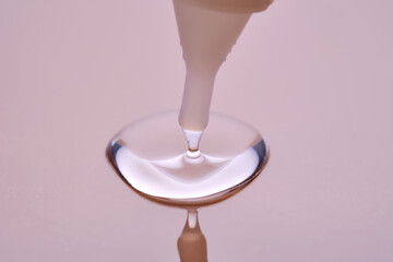 A drop of cosmetic product pours from a tube onto a pink background.