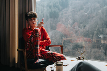 Relaxed individual in red pajamas with a cup of coffee admiring a serene mountain landscape from a...
