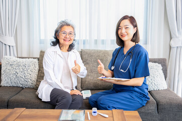 asian senior woman and young female nurse sitting on couch and doing thumb up while a nurse visiting patient at home,concept of elderly health care,home health care,health insurance