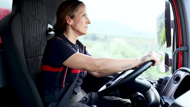 A woman in her 40s and 50s in uniform works as a firefighter.The adult girl is leaving the fire station driving a truck while talking on the radio for an emergency.Concept of working women.