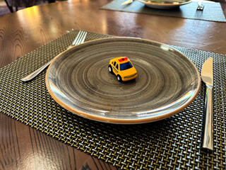 Miniature taxi toy on ceramic plate with cutlery. Concept of calling taxi after end of banquet or celebration. Design of taxi advertising, culinary presentations and unusual concepts.