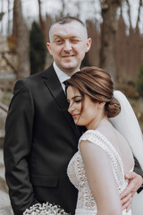 The bride and groom are walking in nature on their wedding day. A man hugs a woman. Zhidka leans tightly against her husband