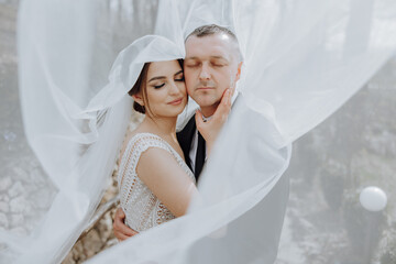 the bride and groom pose under a veil in nature