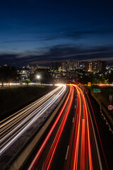 Fototapeta na wymiar Trail of light caused by vehicular traffic in SP-294, Comandante Joao Ribeiro Barros Highway with buildings from downtown in the background, in Marília,