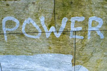 Pressure jet washer used to write the word Power into the grimme on a garden patio showing the difference before and after cleaning