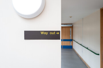 Shallow focus of a Way Out sign seen within an NHS hospital corridor. The door leads to the lobby...