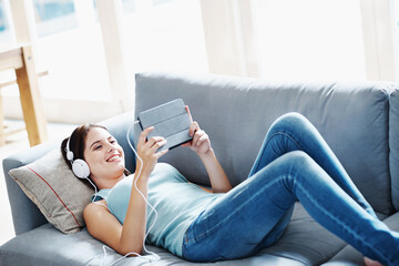 Girl, headphones and tablet on sofa in house for music, streaming and self care while on study...