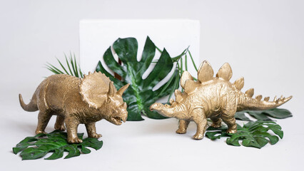 Golden dinosaur figurines and palm leaves on a white background.