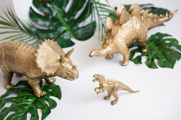 Golden dinosaur figurines and palm leaves on a white background.