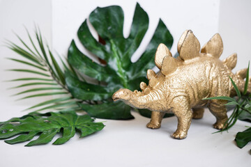 Golden dinosaur figurines and palm leaves on a white background.