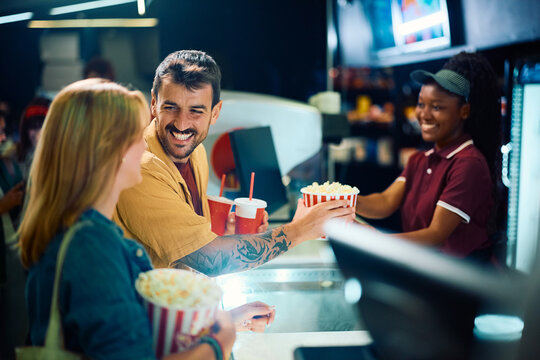 Happy couple buying popcorn and soda at concession stand in movie theater.