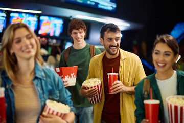 Group of happy friends with popcorn and drinks enjoying in movie theater.
