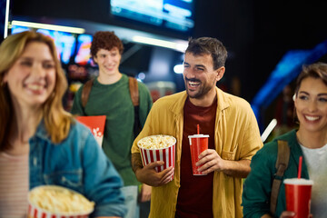 Cheerful man having fun while going on movie projection with friends in cinema.