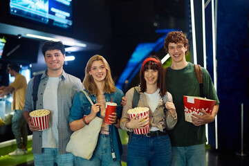 Happy friends with popcorn and drinks in movie theater looking at camera.