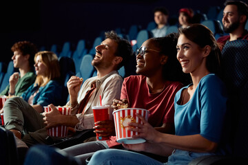 Happy black woman watching comedy movie with friends in cinema.