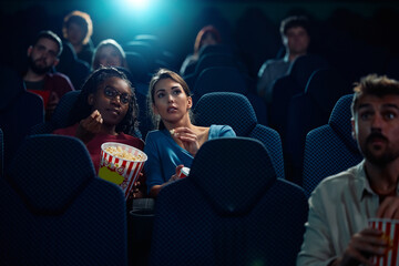 Young women watching suspenseful movie in cinema.