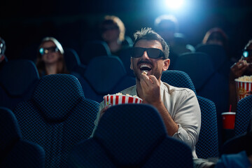 Happy man eating popcorn while watching 3D movie in cinema.