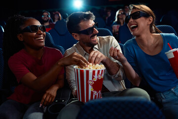 Happy friends laughing and having fun while watching 3D film in movie theater.