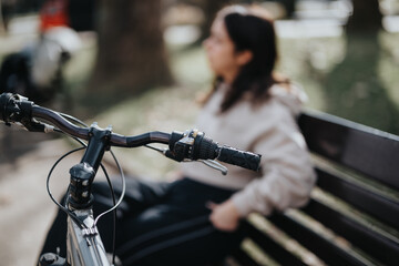 Close-up of bicycle handle and a relaxed woman sitting on a park bench, enjoying nature