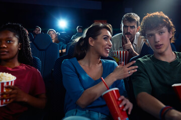 Annoyed man shushing  couple who is talking during movie projection in cinema.