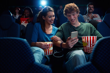 Happy couple texting on mobile phone during film screening in movie theater.