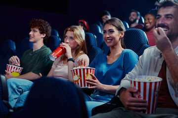 Happy woman eating popcorn while watching movie with friends in cinema.